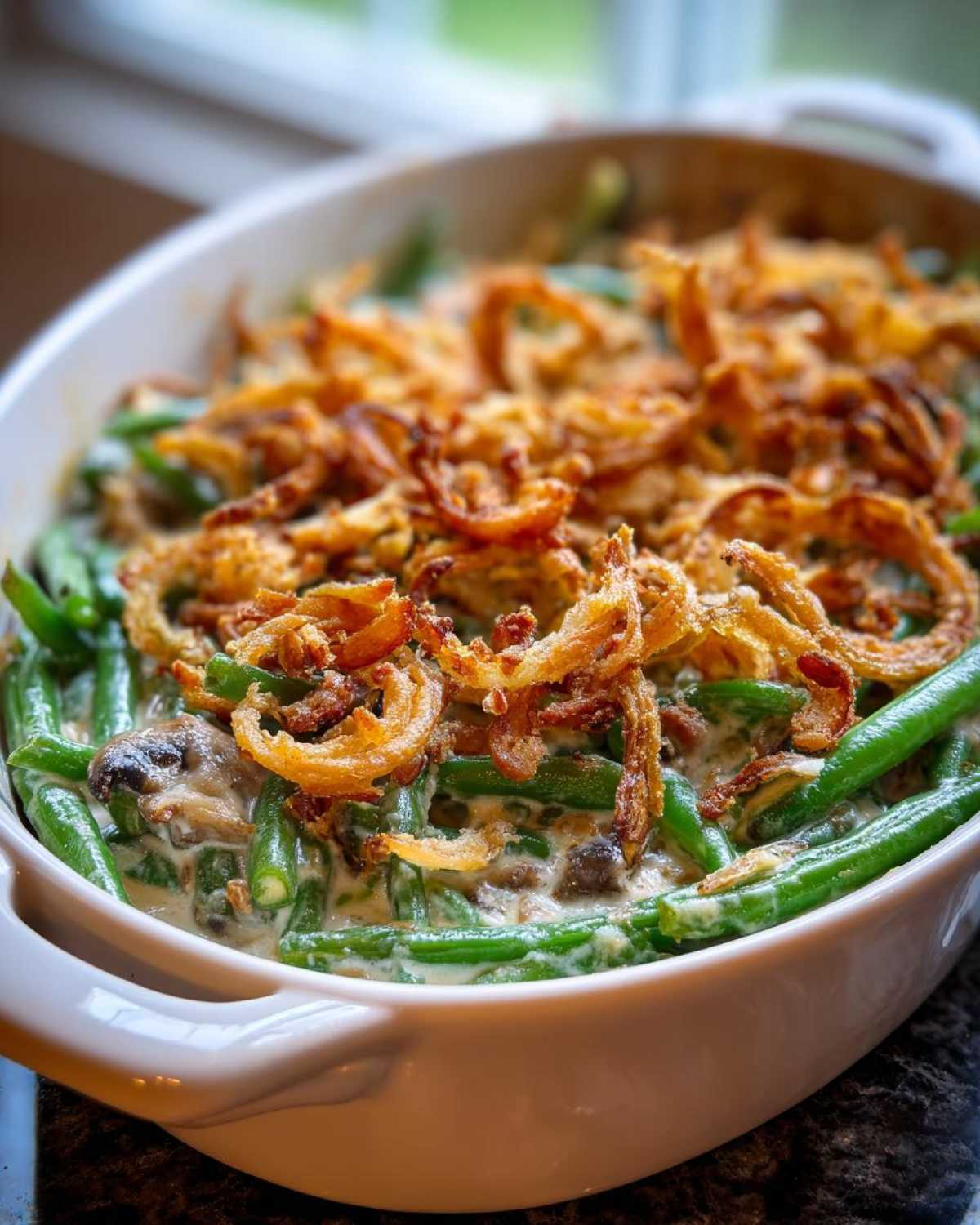 Close-up of a white bowl filled with creamy green bean casserole topped generously with crispy fried onions.