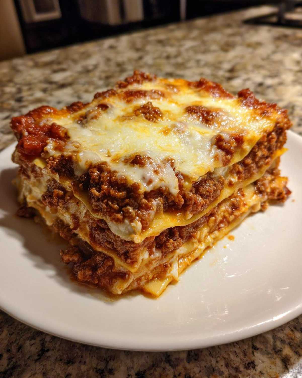 A hearty, multi-layered slice of amazing lasagna with rich meat sauce and melted mozzarella cheese on a white plate.