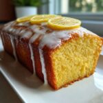 A whole, moist lemon pound cake drizzled with white glaze and topped with thin lemon slices.