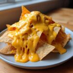 A pile of tortilla chips generously smothered in thick, bright yellow nacho cheese sauce.