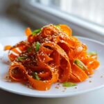 Close-up of vibrant raw carrot salad ribbons tossed in dressing and topped with sesame seeds and green onions.
