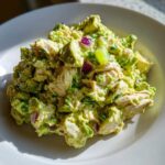 A mound of fresh avocado chicken salad featuring chunks of chicken, avocado, red onion, and celery on a white plate.