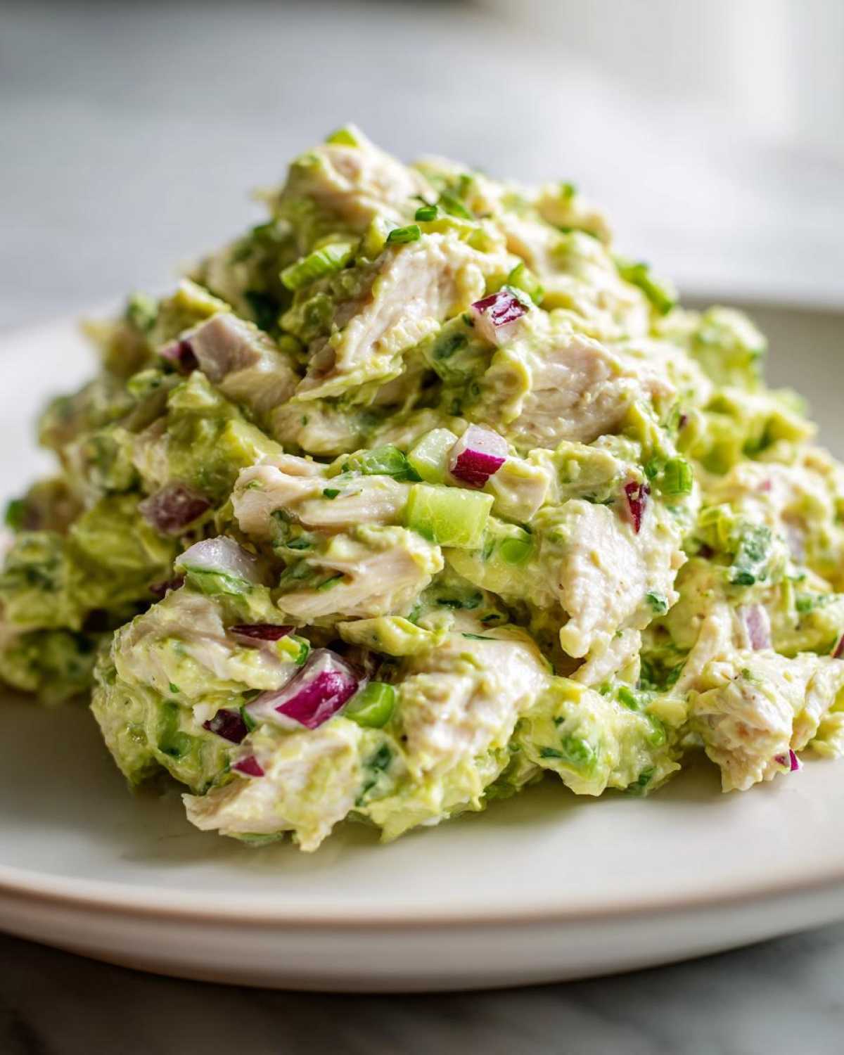 Close-up of a mound of fresh avocado chicken salad featuring chunks of chicken, red onion, and celery.
