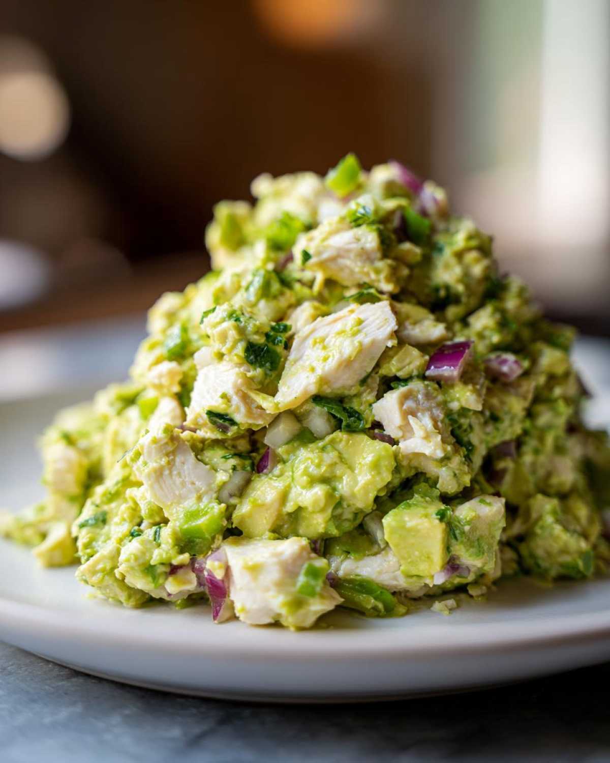 A mound of creamy avocado chicken salad featuring chunks of white chicken, mashed avocado, and diced red onion.