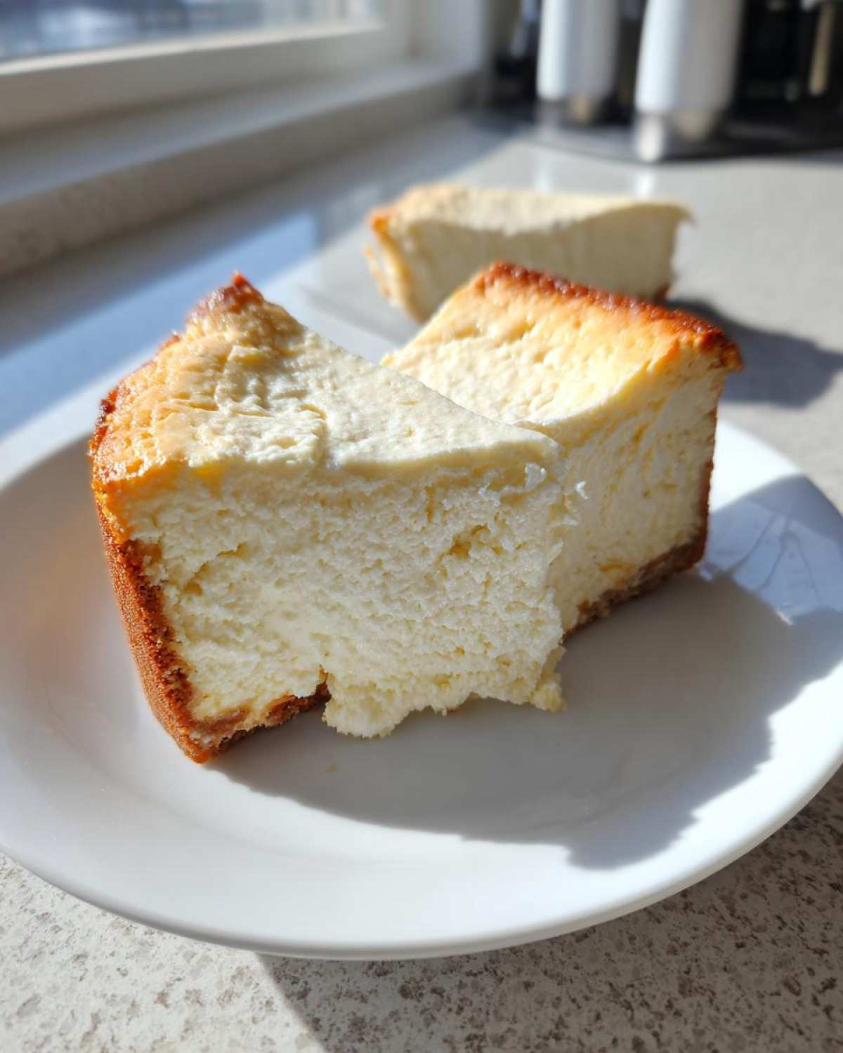 Close-up of a thick slice of baked Protein Cheesecake with a golden brown edge, served on a white plate.
