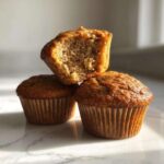 Three moist banana protein muffins stacked, one cut open showing the fluffy interior texture.