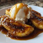 Close-up of caramelized bananas foster topped with a scoop of vanilla ice cream and drizzled with caramel sauce.