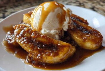 Close-up of caramelized bananas foster topped with a scoop of vanilla ice cream and drizzled with caramel sauce.