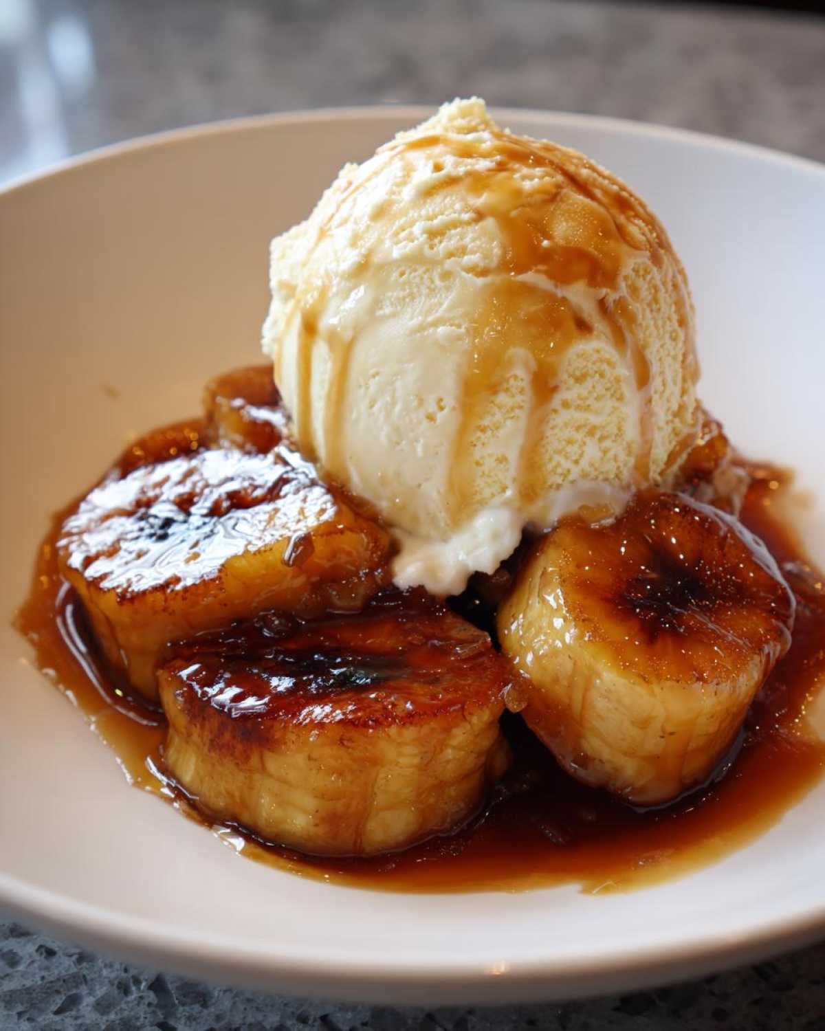 Close-up of caramelized bananas foster topped with melting vanilla ice cream and caramel sauce.