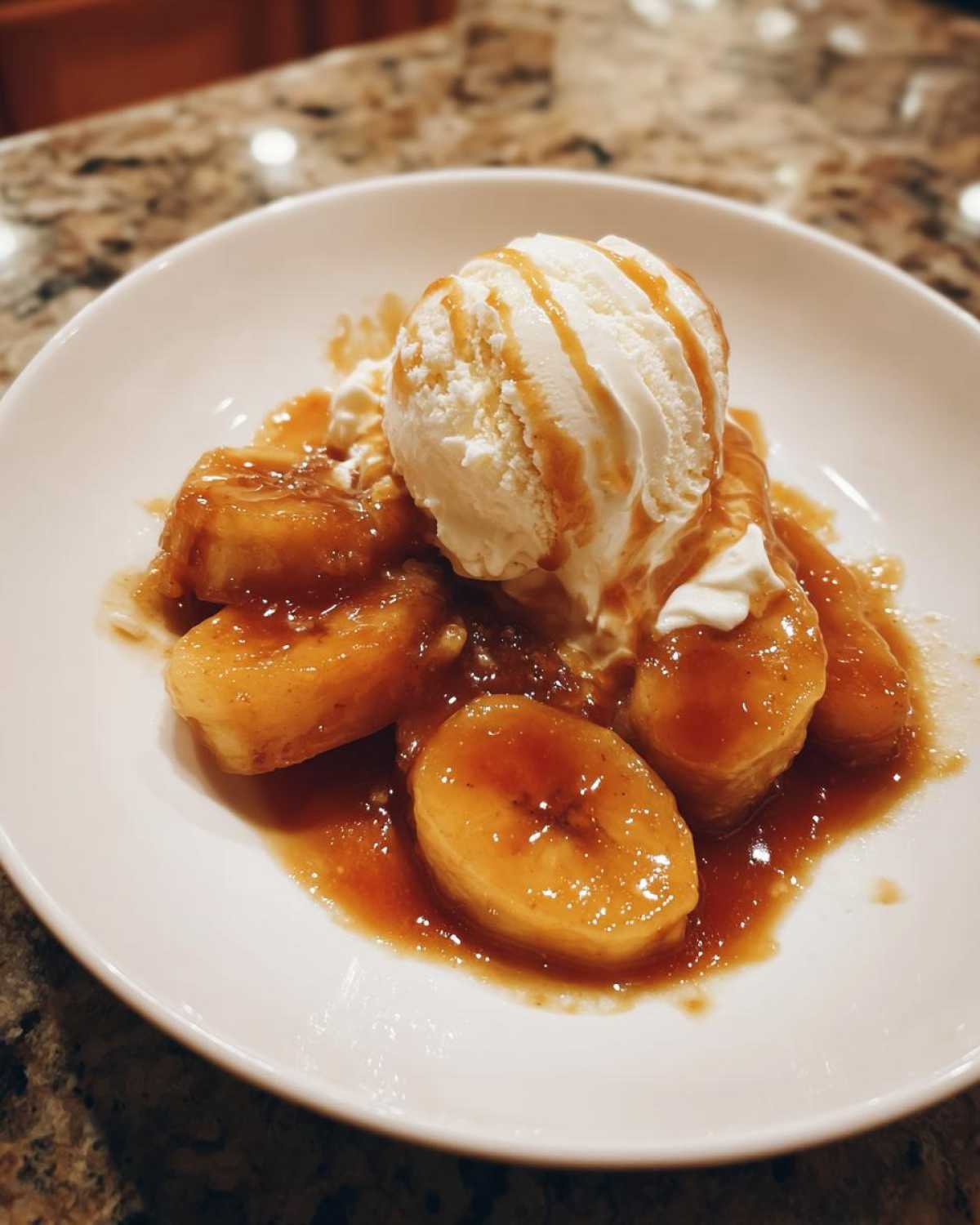 Close-up of Bananas Foster: caramelized bananas in rich sauce topped with vanilla ice cream and caramel drizzle.