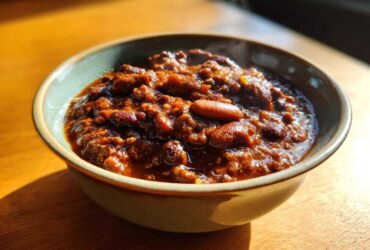 Close-up of a steaming bowl filled with rich, dark red chili, featuring beans and ground meat.