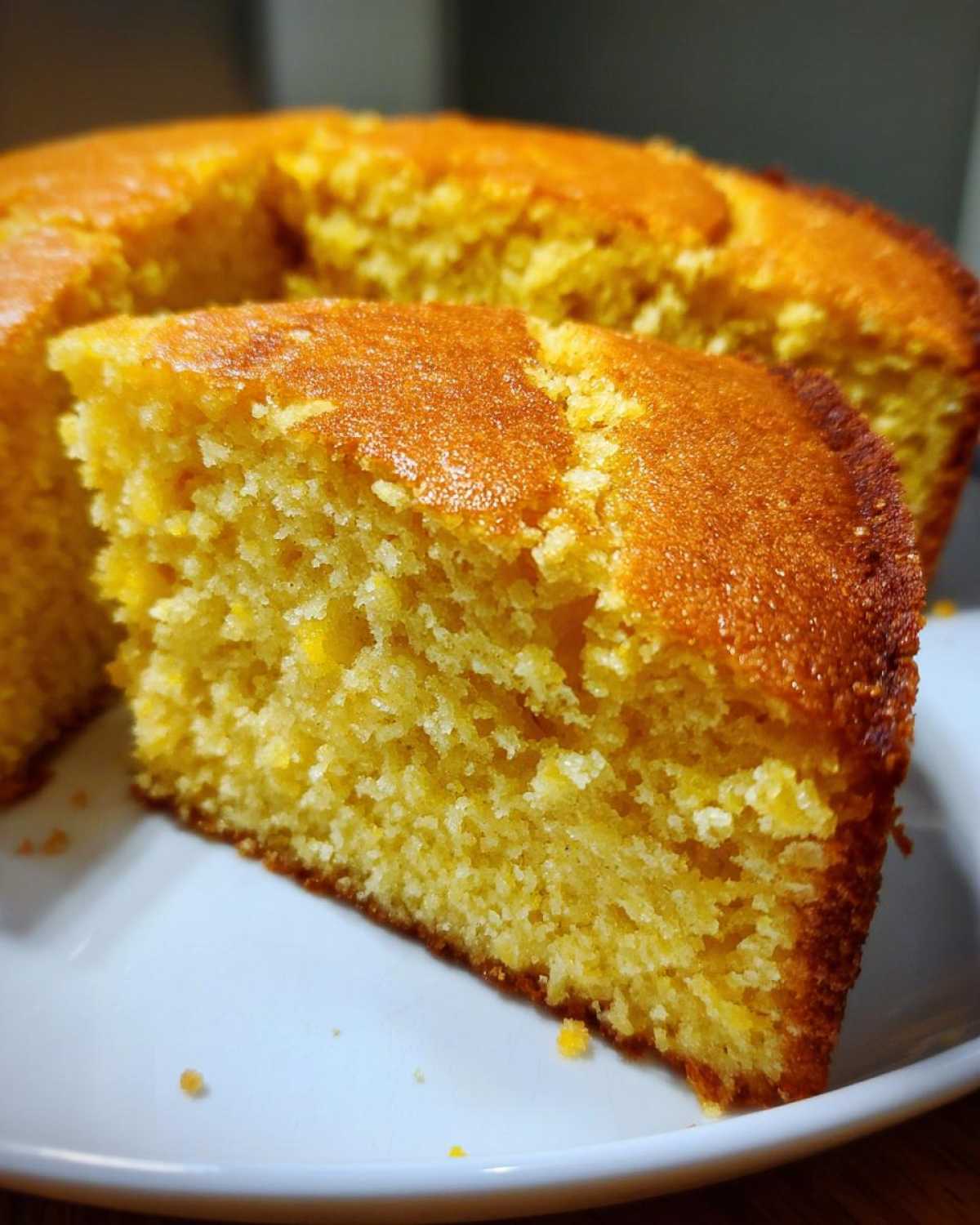 A close-up of a moist, golden slice of buttermilk cornbread with a slightly browned crust, resting on a white plate.