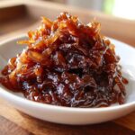 A close-up of rich, dark brown caramelized onions piled high in a small white bowl.