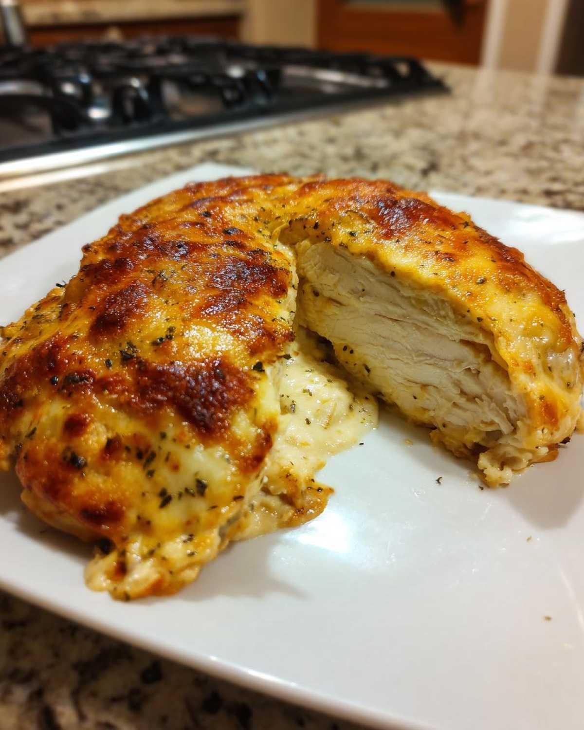 A caesar chicken breast, cut in half to show the cooked white meat and melted cheesy topping.