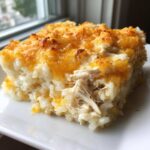 A square serving of cheesy chicken and rice casserole topped with melted, golden cheddar cheese.