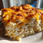 A close-up serving of cheesy chicken and rice casserole showing shredded chicken, creamy rice, and a bubbly, browned cheddar cheese topping.
