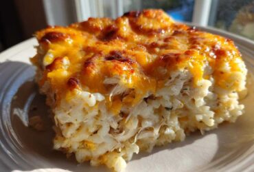 A close-up serving of cheesy chicken and rice casserole showing shredded chicken, creamy rice, and a bubbly, browned cheddar cheese topping.