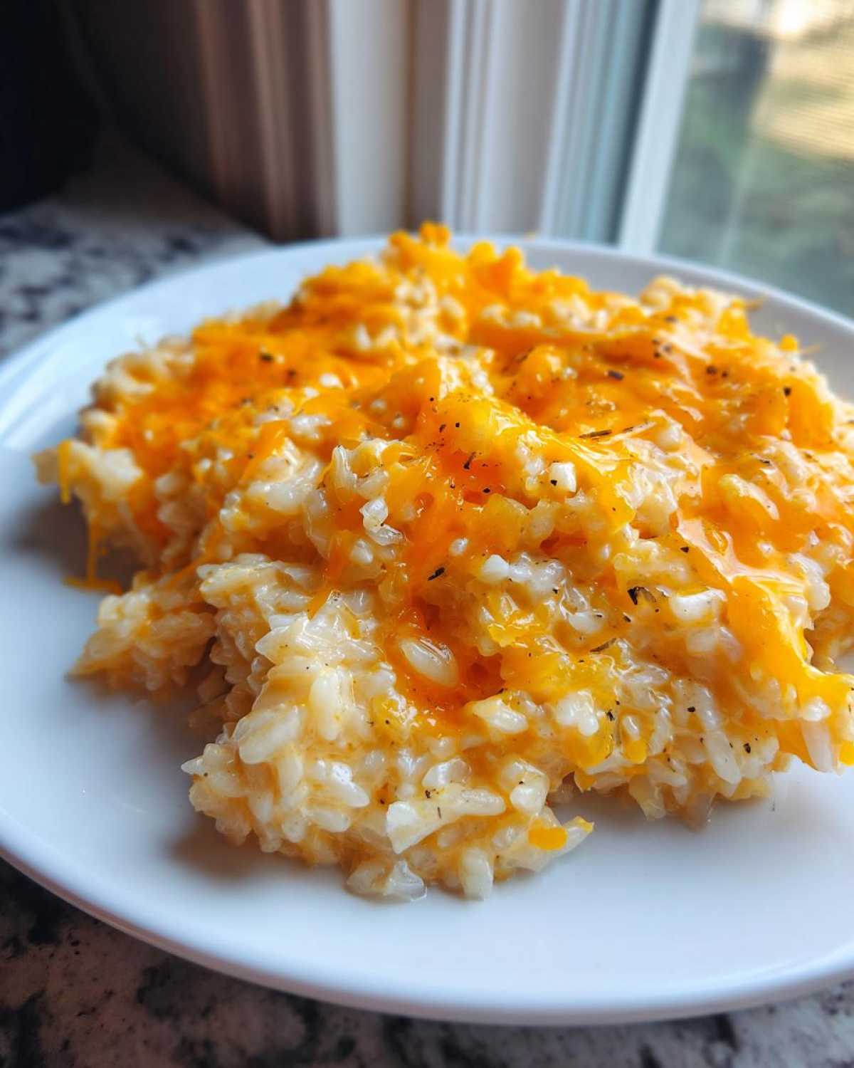 A close-up of creamy cheesy rice topped with melted orange cheddar cheese and black pepper.