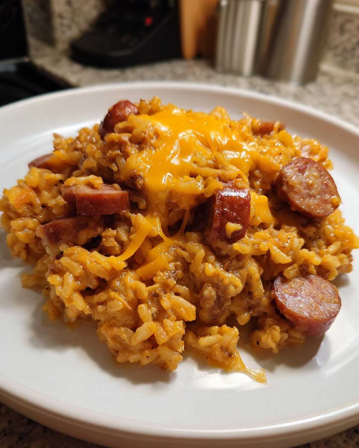A serving of cheesy sausage and rice topped with melted cheddar cheese on a white plate.
