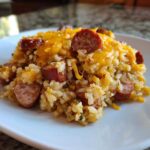 A close-up of a serving of cheesy sausage and rice, topped with melted cheddar cheese.