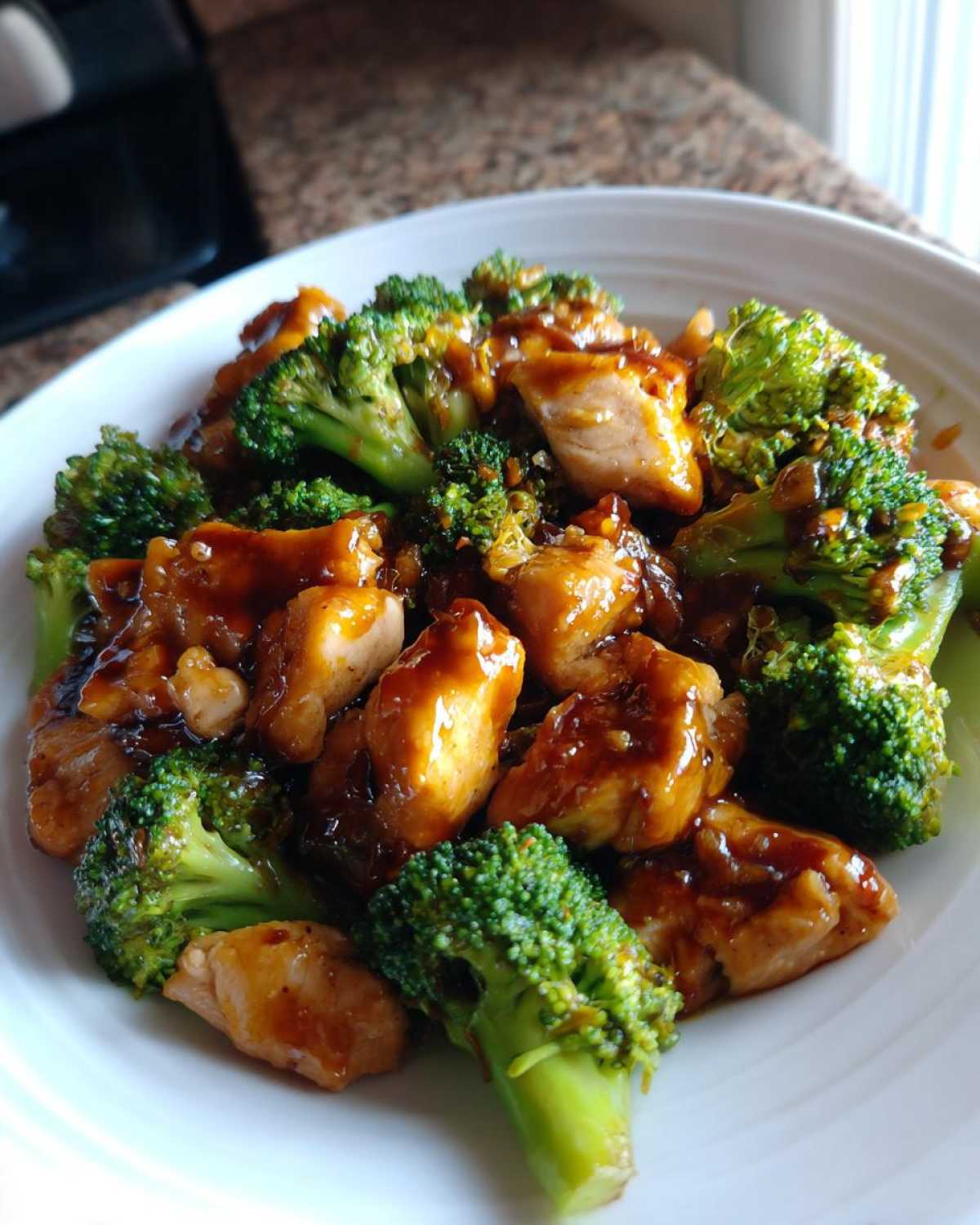 A close-up of tender chicken pieces and bright green broccoli florets coated in a savory brown sauce, featuring chicken and broccoli.