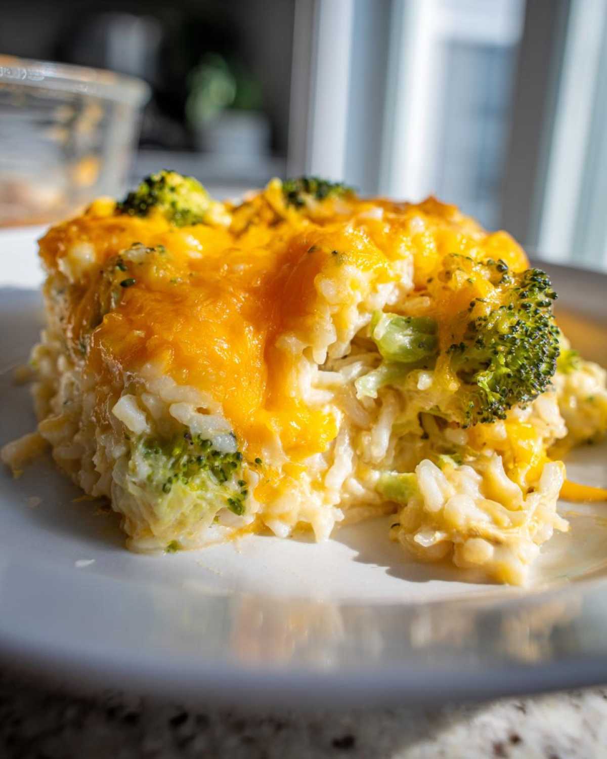 A close-up of a portion of chicken broccoli rice casserole topped with melted cheddar cheese.