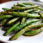 Close-up of vibrant green beans coated in a savory garlic sauce, ready to serve.