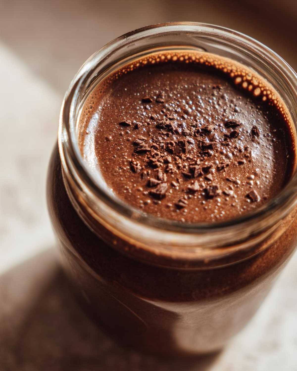 Overhead close-up of creamy chocolate overnight oats topped with chocolate shavings in a glass jar.
