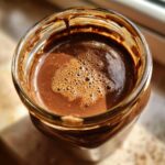 Overhead close-up of rich, foamy chocolate overnight oats mixture in a glass jar.