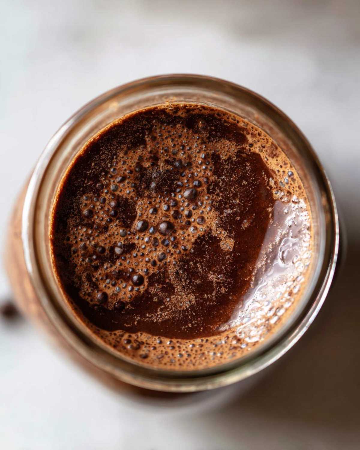 Overhead close-up of the rich, frothy, dark brown liquid mixture for chocolate overnight oats in a glass jar.