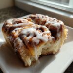A close-up of a serving of gooey Cinnamon roll casserole topped with thick white icing.