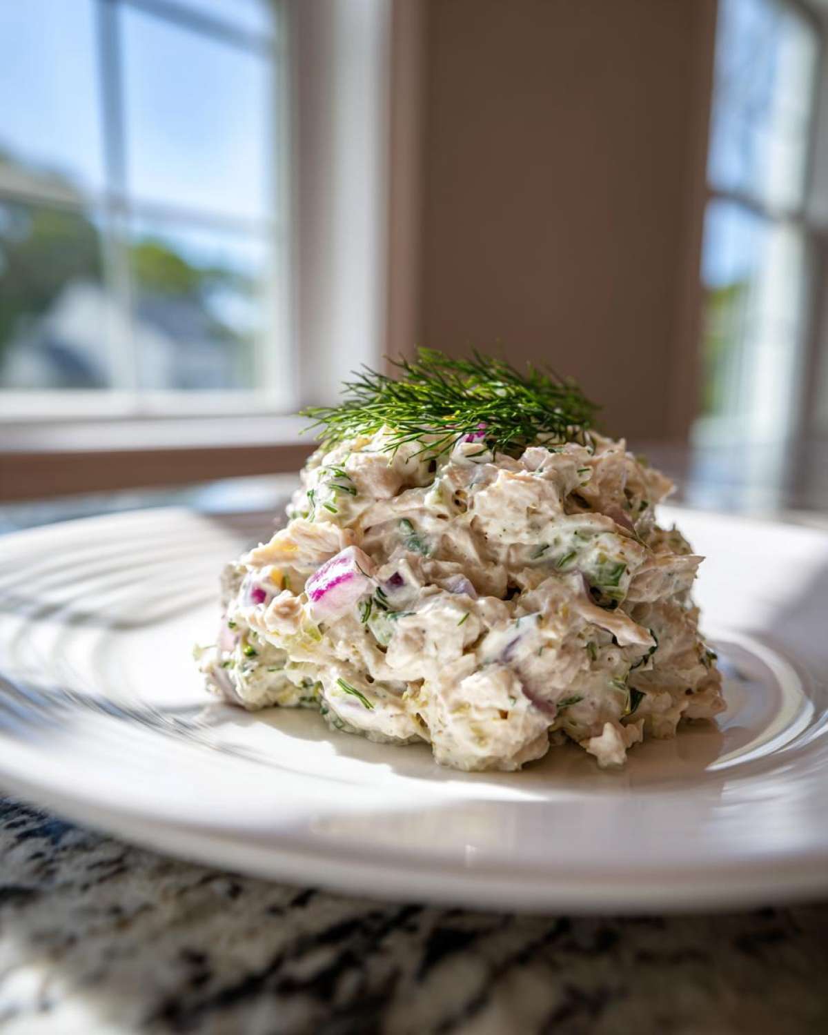 A mound of creamy cottage cheese chicken salad mixed with red onion and topped with fresh dill, served on a white plate.