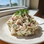 A mound of creamy cottage cheese chicken salad mixed with red onion and celery, topped with fresh dill.