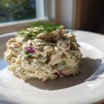 A scoop of creamy cottage cheese chicken salad mixed with red onion and herbs, topped with fresh dill.
