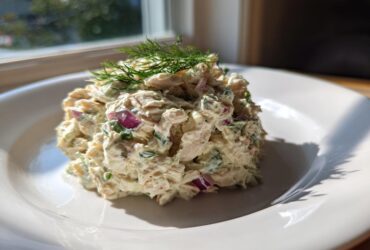 A scoop of creamy cottage cheese chicken salad mixed with red onion and herbs, topped with fresh dill.