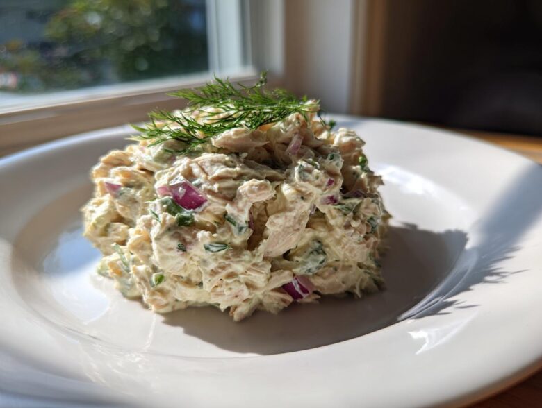 A scoop of creamy cottage cheese chicken salad mixed with red onion and herbs, topped with fresh dill.