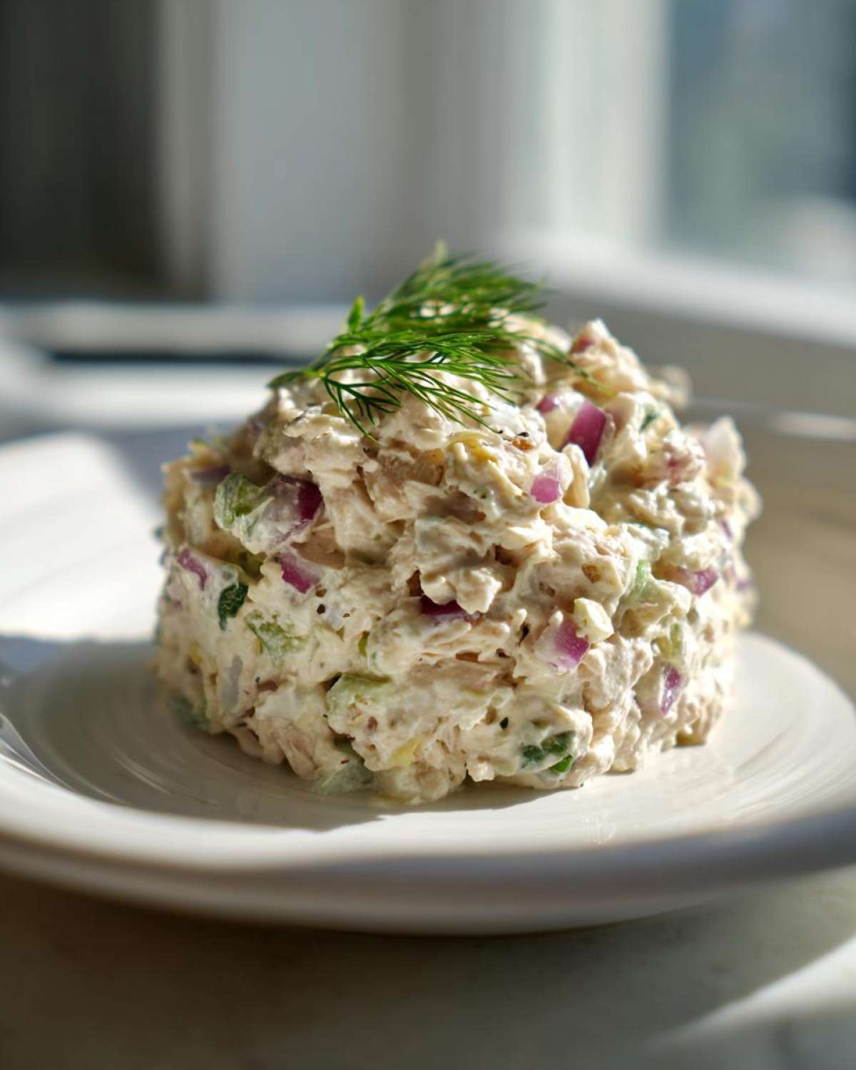 A mound of creamy cottage cheese chicken salad mixed with red onion and celery, garnished with fresh dill.