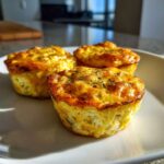 Three golden brown cottage cheese egg cups starbucks style, sprinkled with herbs, sitting on a white plate.
