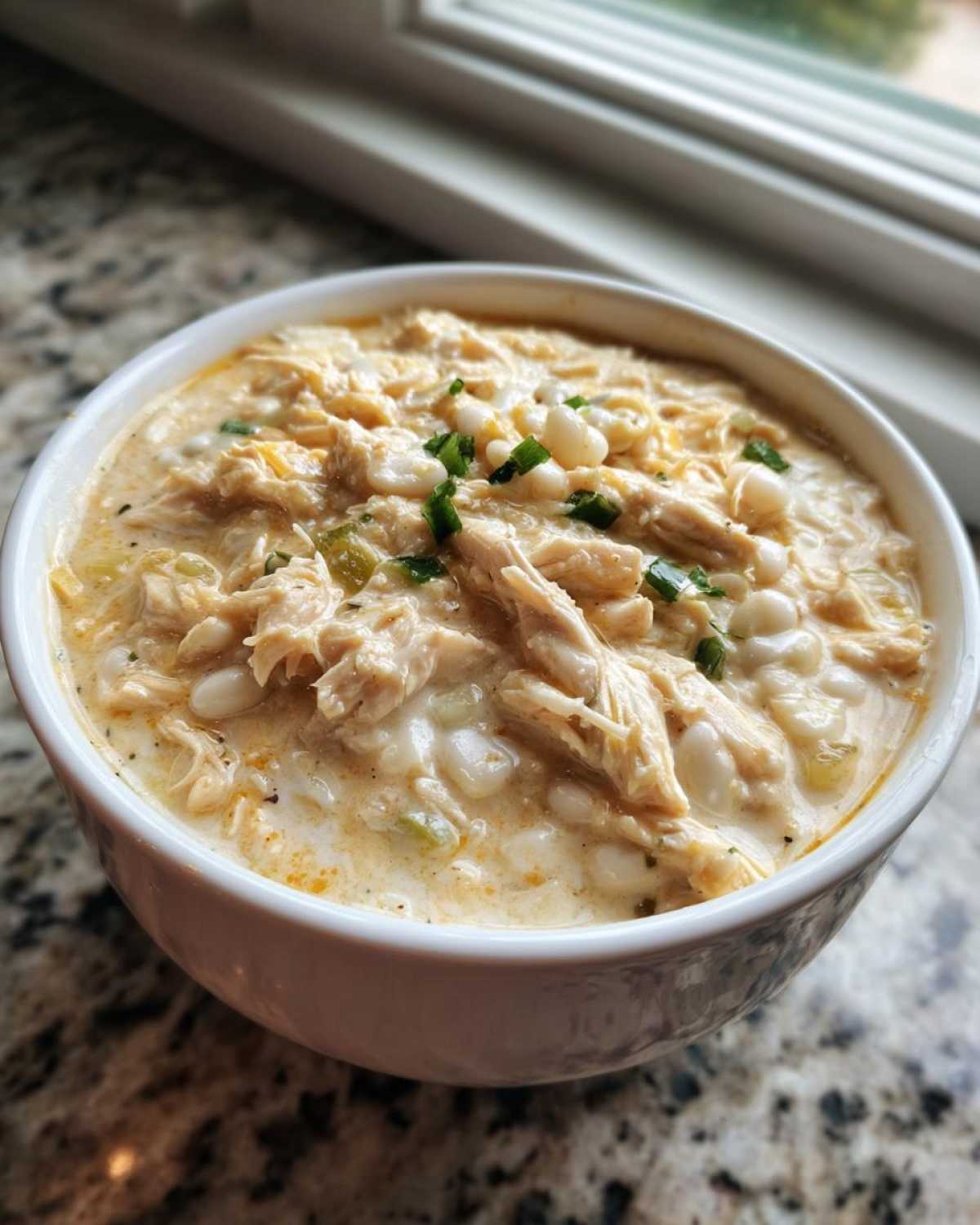 Close-up of a white bowl filled with creamy crockpot white chicken chili, topped with green onions.