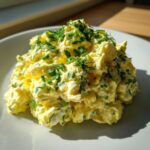 A mound of creamy, yellow egg salad recipe garnished generously with chopped chives and dill.