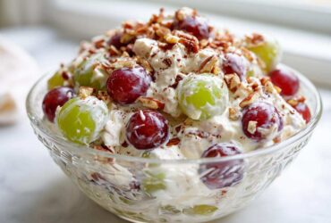 A close-up of creamy grape salad, featuring red and green grapes mixed with a sweet cream dressing and topped with chopped pecans.