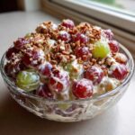 Close-up of a bowl of creamy grape salad, featuring red and green grapes coated in dressing and topped with chopped pecans, similar to chicken salad chick grape salad.