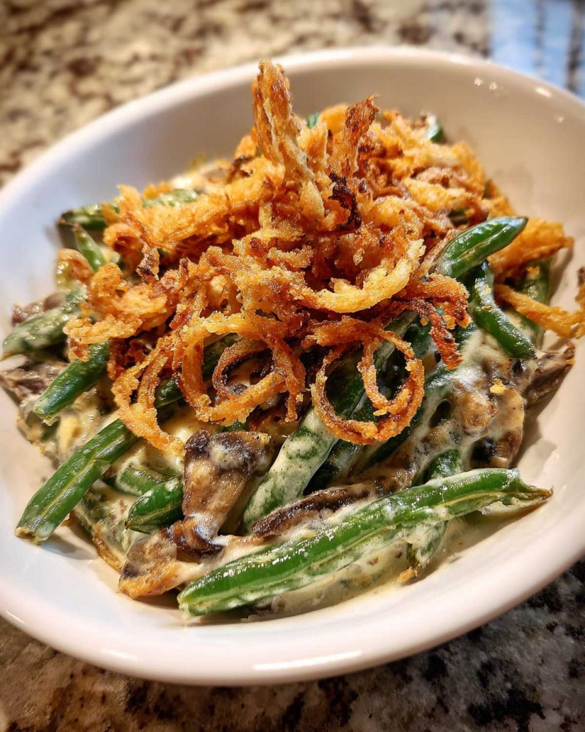 A close-up of a serving of creamy green bean casserole topped generously with crispy fried onions.