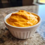 Close-up of thick, bright orange homemade nacho cheese sauce served in a small white fluted ramekin.