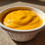 A close-up of thick, bright orange homemade nacho cheese sauce served in a small white bowl.