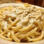 Close-up of fettuccine pasta generously coated in rich, creamy olive garden alfredo sauce and topped with pepper.