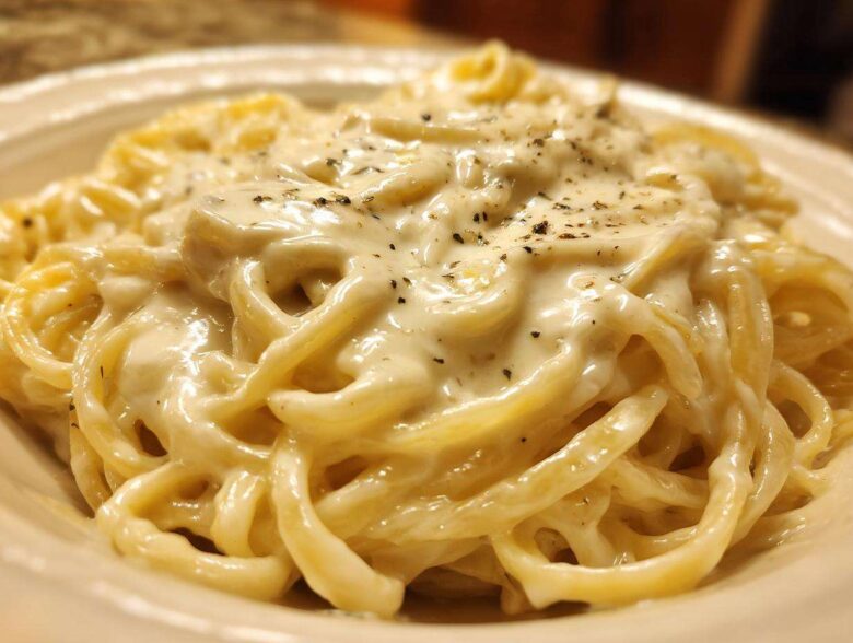 Close-up of fettuccine pasta generously coated in rich, creamy olive garden alfredo sauce and topped with pepper.