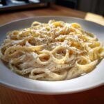 Close-up of fettuccine pasta coated in rich homemade alfredo sauce and topped with cracked black pepper.