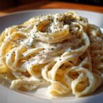 Close-up of fettuccine pasta generously coated in rich homemade alfredo sauce and sprinkled with herbs.