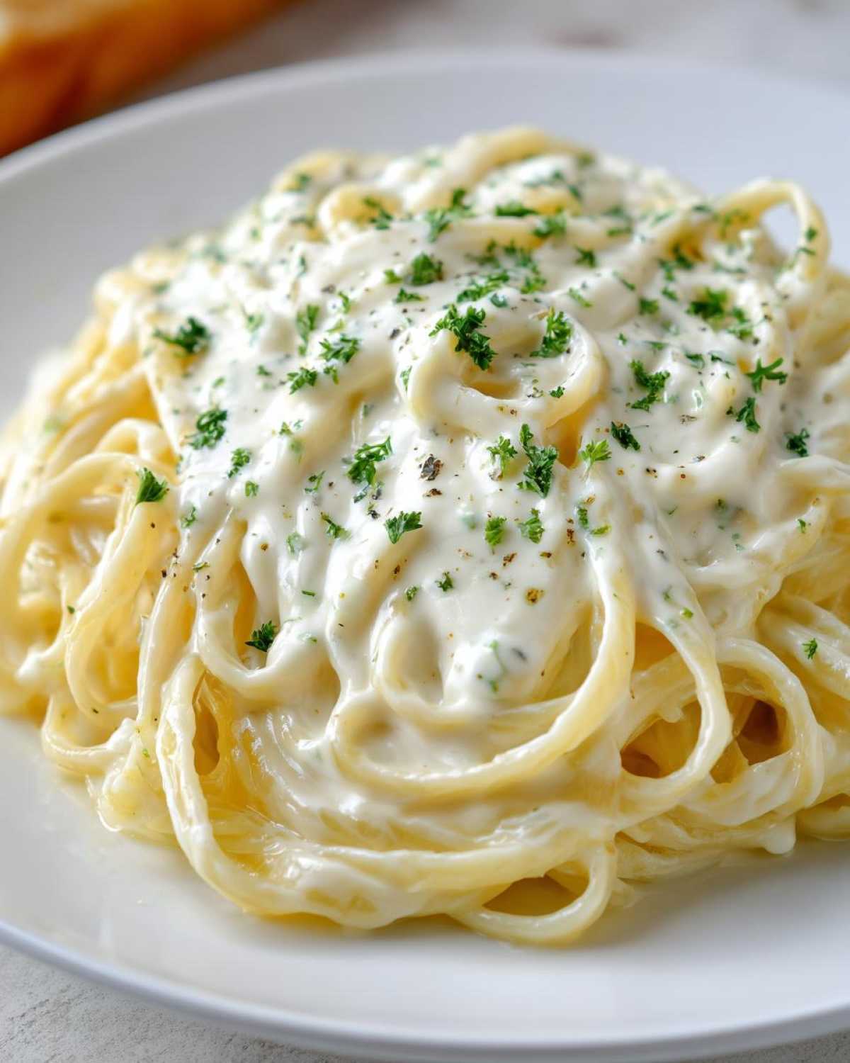 Close-up of fettuccine pasta generously coated in rich homemade alfredo sauce and topped with fresh parsley.